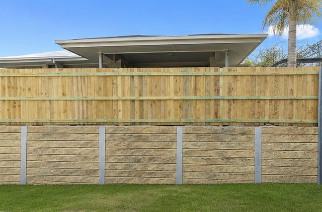 A timber and concrete-block boundary fence beside a maintained lawn