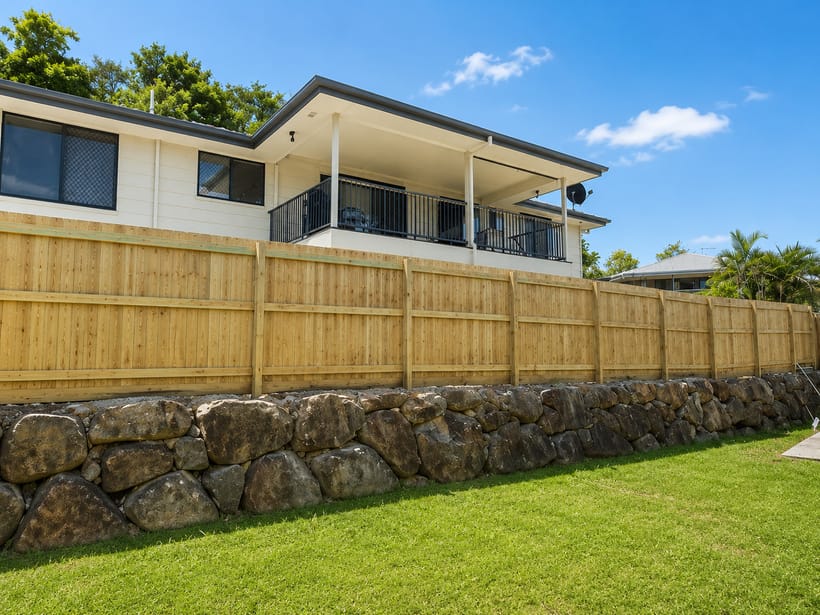 A newly built timber fence on a stone retaining wall beside a tidy lawn at a Brisbane home